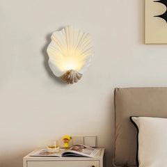 Shell-shaped wall light fixture on a bedroom wall with a nightstand and bed in the foreground.