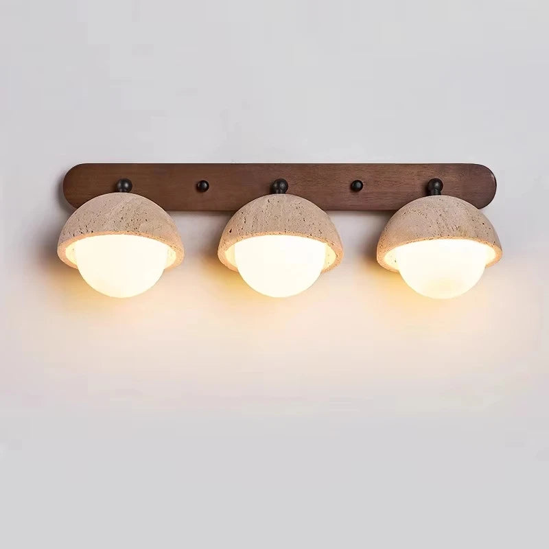 “Three-light travertine stone wall lamp mounted on a wood bar with warm glow.”