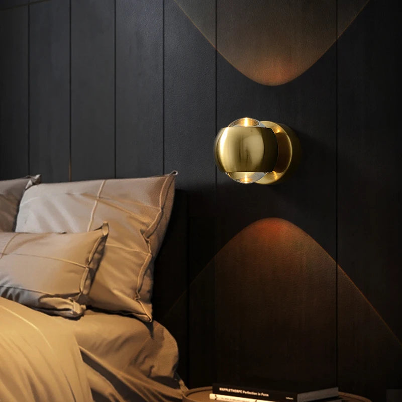 Gold circular light fixture on a dark wooden wall with pillows and bedding.