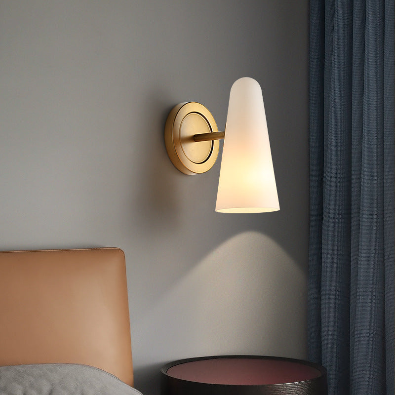 Wall-mounted lamp with a cone-shaped shade on a gray wall next to a bed.